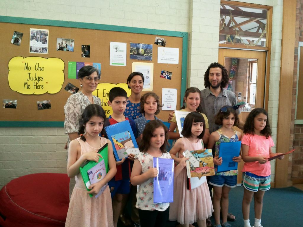 ALCASA Children Group with ALCASA leaders, children are holding folders showcasing their work and Arabic books